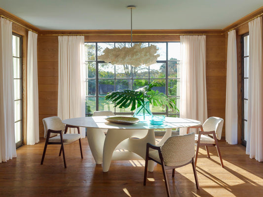 Dining room with white floor-length curtains on wood-paneled walls and a sculptural table