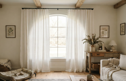 Modern farmhouse living room with sheer white linen curtains framing an arched window under rustic wood beams
